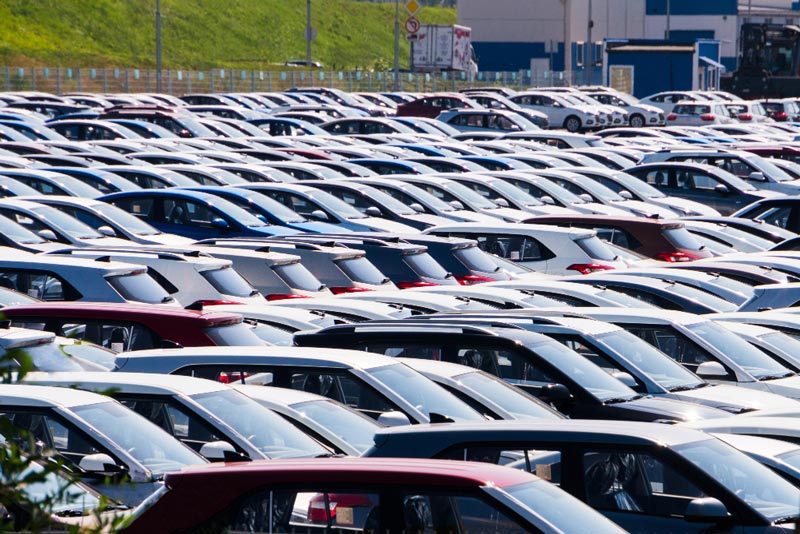 Ein dicht bepackter Parkplatz bei Gebrauchtwagen Ankauf Steinfurt ist mit Reihen geparkter Autos in verschiedenen Farben, hauptsächlich Weiß und Rot, unter einem sonnigen blauen Himmel gefüllt.