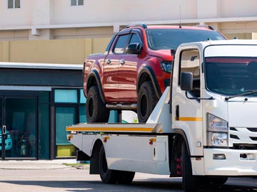 Ein rotes Pickup wird in einer sonnigen städtischen Umgebung auf einen weißen Abschleppwagen von Unfallwagenankauf Steinfurt verladen.